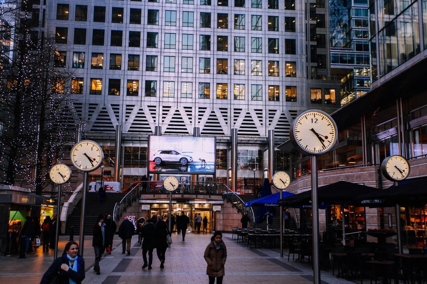 Street clocks and office towers at Canary Wharf, the London financial district, at dusk